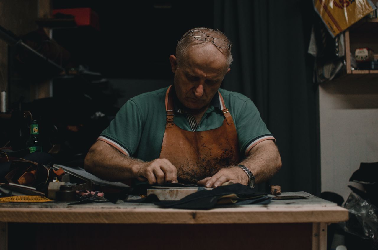 Focused leather artisan in a leather apron working at a traditional workshop bench