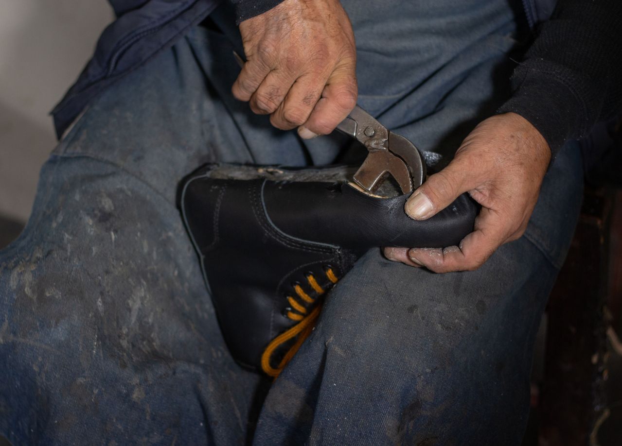 Hands using lasting pincers to shape leather on a black boot
