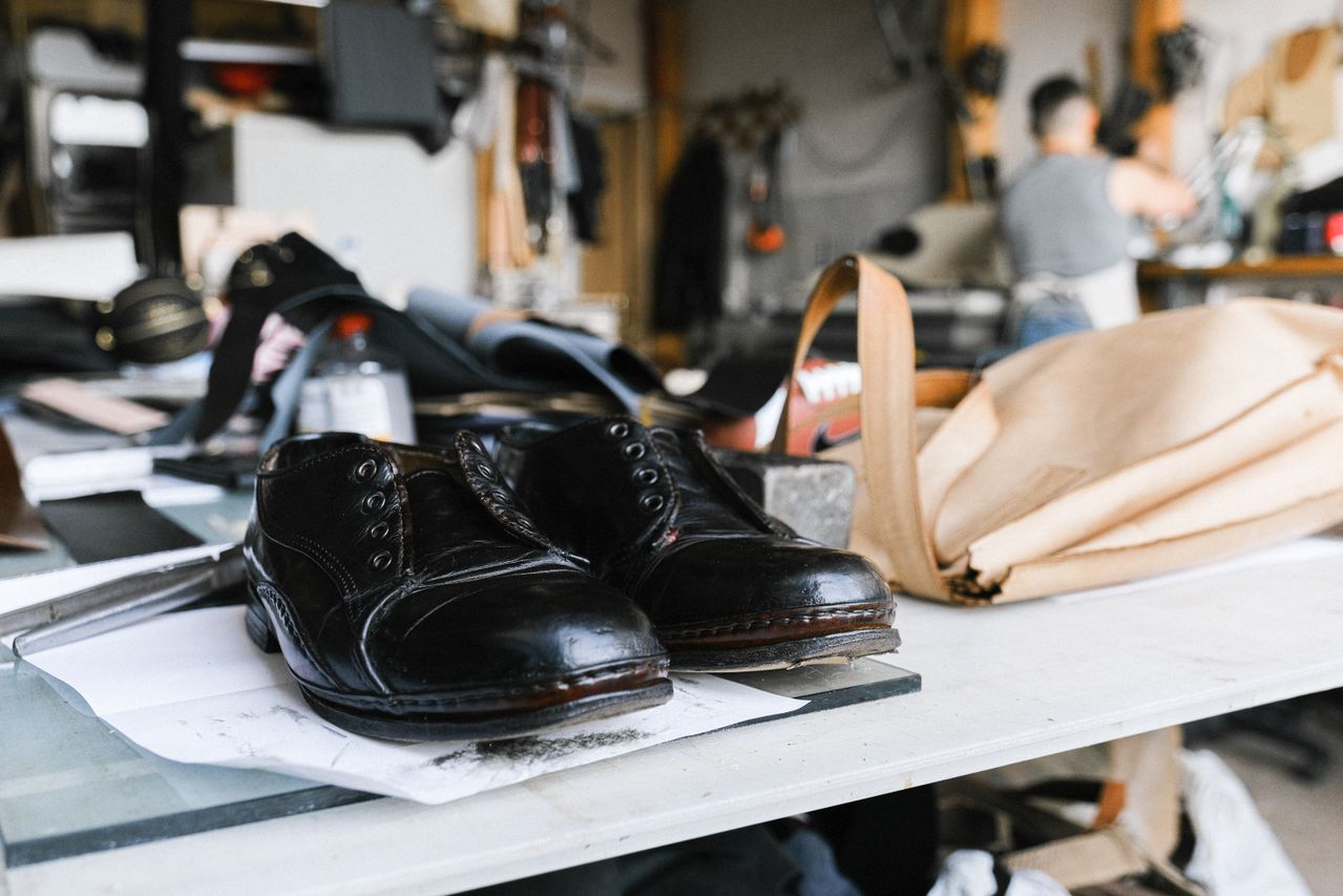 Black leather dress shoes resting on a workshop bench beside leather tools
