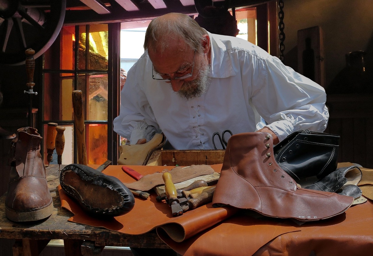 Master craftsman working leather and wooden lasts at a sunlit atelier workbench