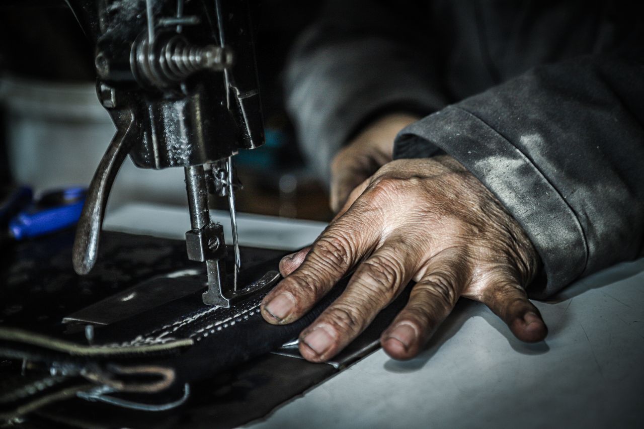 Close-up of a craftsman stitching dark leather on a heavy-duty sewing machine
